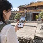 Du khách đeo tai nghe nghe audio guide di tích qua điện thoại cạnh biển mã QR khắc trên bệ đá